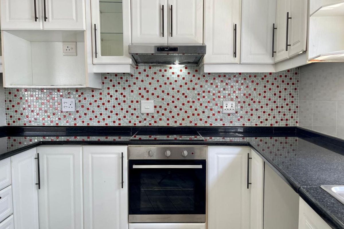 A clean, functional kitchen featuring white shaker-style cabinetry, black granite countertops, and a decorative red and white mosaic tile backsplash with integrated appliances.