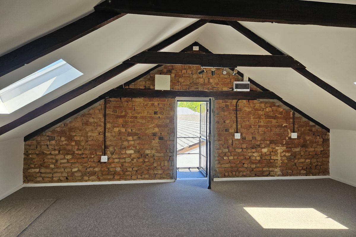 Spacious attic bedroom featuring exposed brick walls, timber ceiling beams, and skylights, offering a unique industrial-style living space with direct outdoor access.