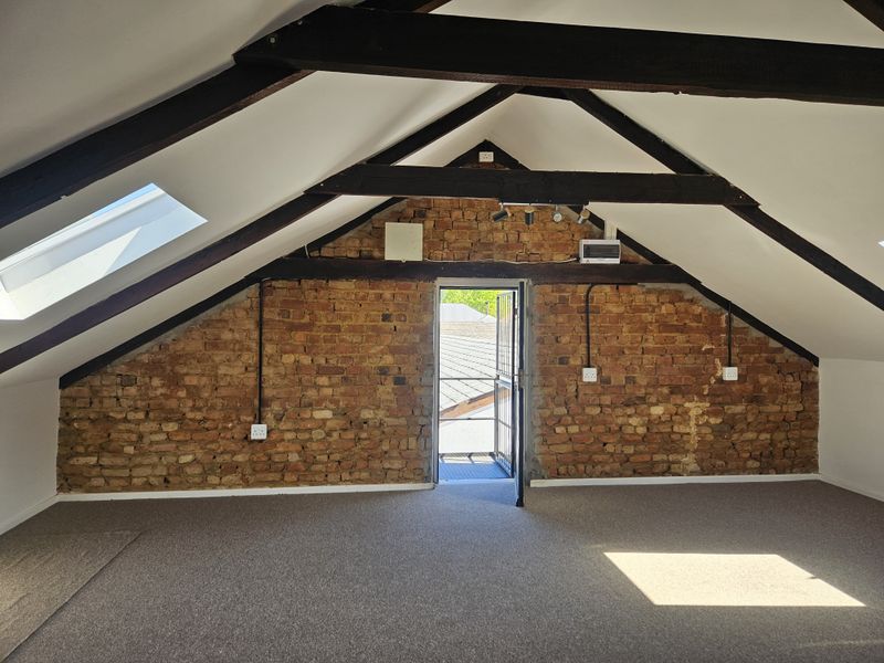 Spacious attic bedroom featuring exposed brick walls, timber ceiling beams, and skylights, offering a unique industrial-style living space with direct outdoor access.