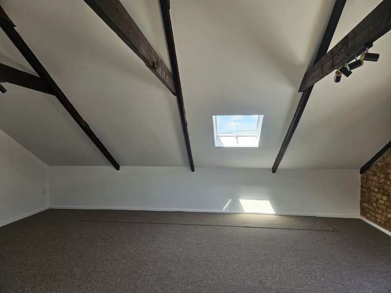 Spacious attic bedroom featuring exposed timber beams, a skylight, and an exposed brick feature wall, offering a bright and characterful living space.