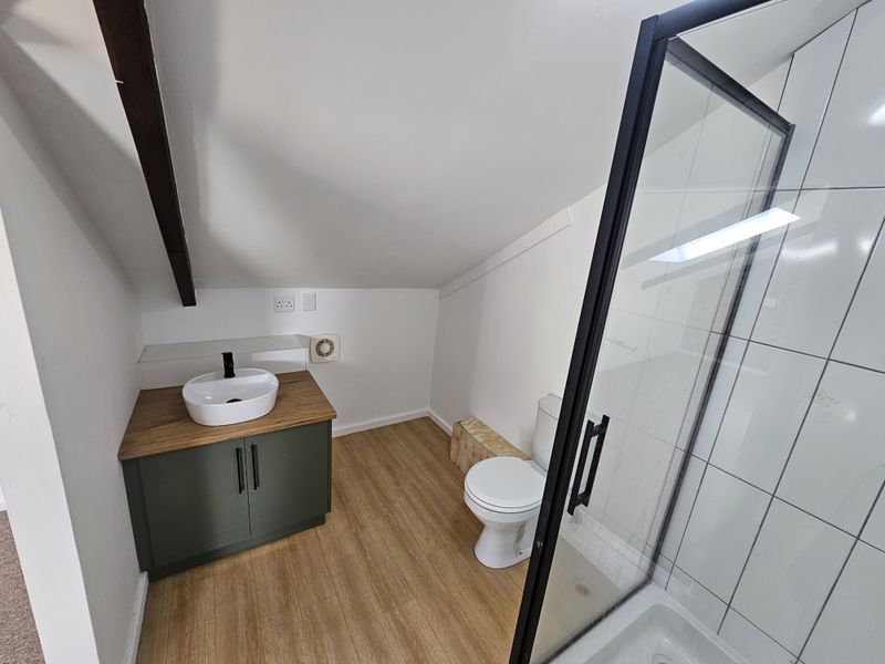 Modern bathroom featuring a vanity with a vessel sink, a glass-enclosed shower, and wood-look laminate flooring under a sloped ceiling.