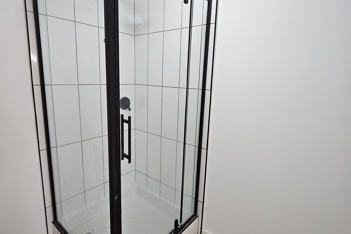 A modern bathroom featuring a corner shower enclosure with black framing, white tiled walls, and wood-look laminate flooring.