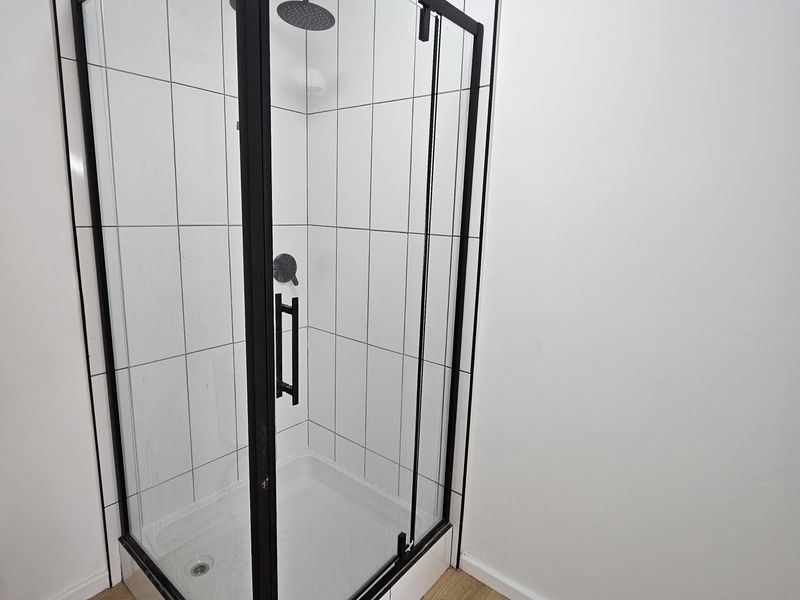 A modern bathroom featuring a corner shower enclosure with black framing, white tiled walls, and wood-look laminate flooring.