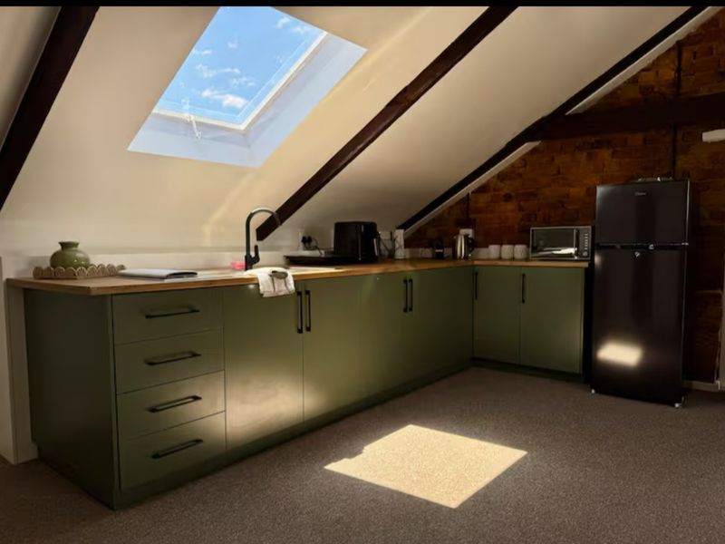 A modern attic kitchen featuring olive green cabinetry, wooden countertops, exposed brickwork, and a large skylight providing natural light.
