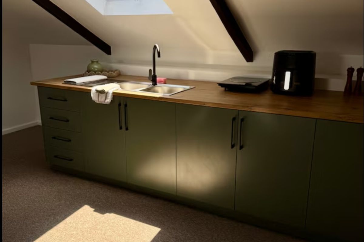 A compact attic kitchen featuring olive green cabinetry, a wooden countertop, stainless steel sink, and a skylight providing natural light.