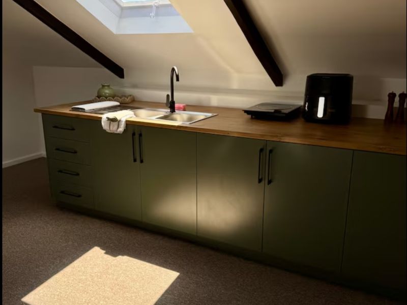 A compact attic kitchen featuring olive green cabinetry, a wooden countertop, stainless steel sink, and a skylight providing natural light.