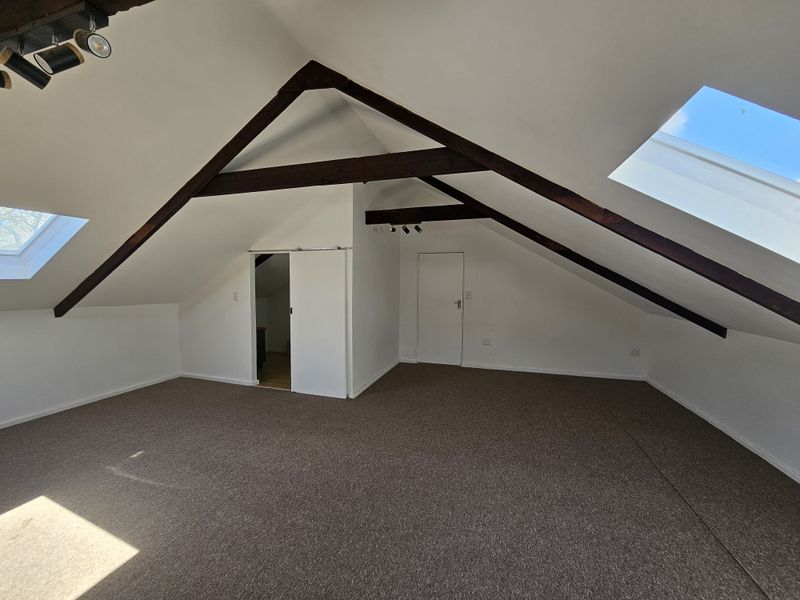 Spacious attic bedroom featuring exposed timber beams, skylight windows, and neutral carpeting, offering a bright and versatile living space.