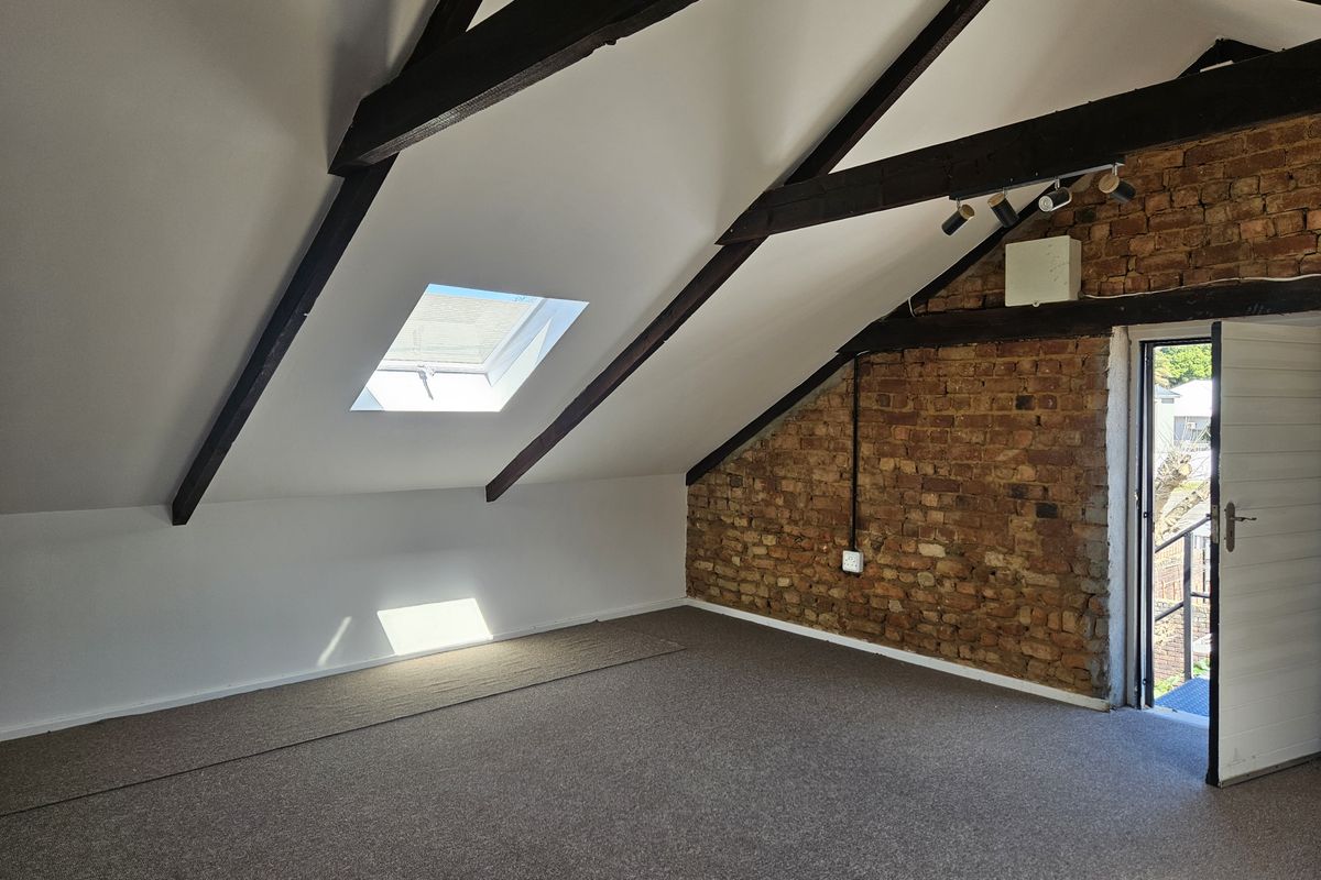 Spacious attic bedroom featuring exposed timber beams, a skylight, and a characterful exposed brick wall with direct access to an outdoor area.