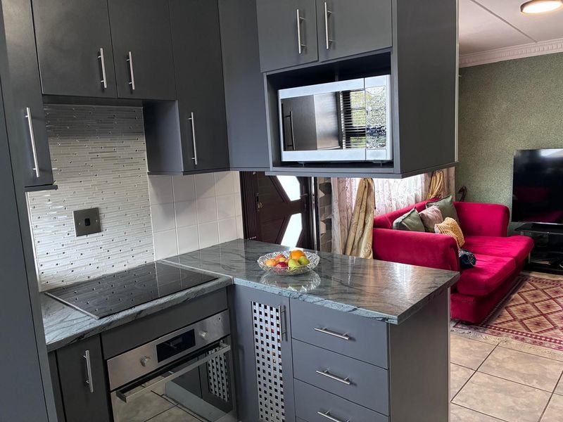 Modern open-plan kitchen featuring dark grey cabinetry, stone countertops, integrated oven, hob, and microwave, seamlessly flowing into the adjacent living area.