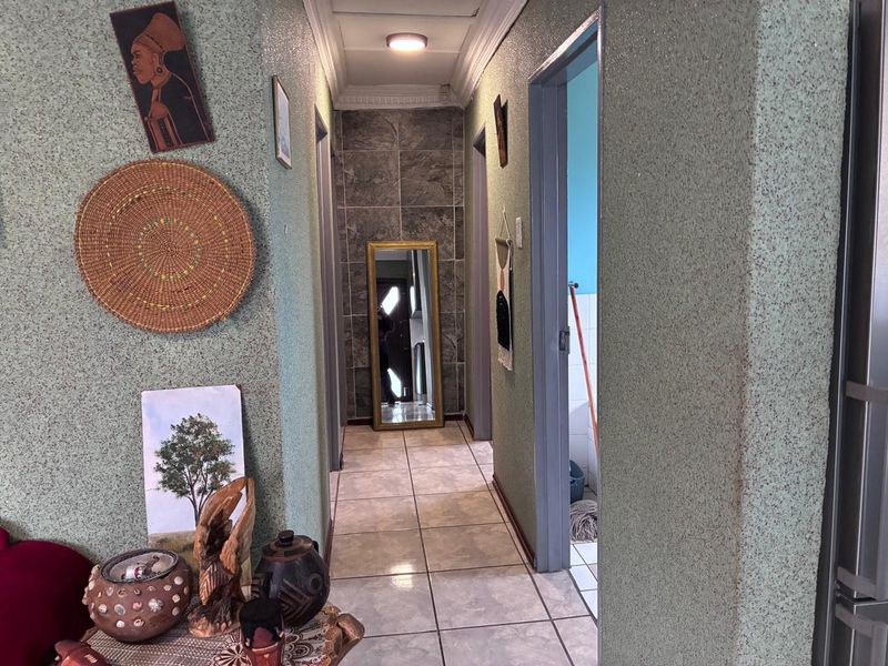 A residential hallway featuring textured wall finishes, ceramic floor tiling, and a tiled feature wall at the end of the passage.
