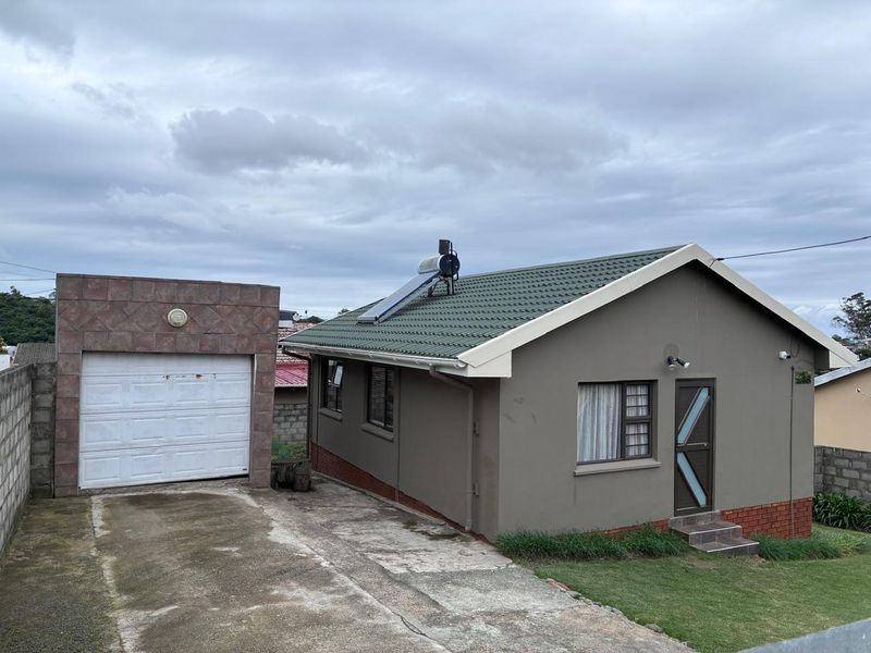 A detached house featuring a tiled roof with a solar water heater, a single garage, and a concrete driveway, set within a fenced property.