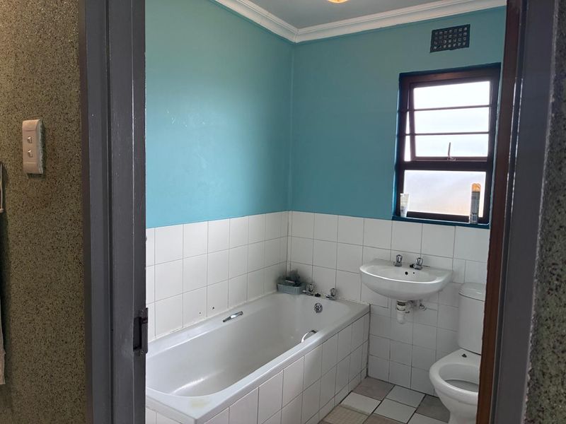 A dated bathroom featuring a built-in bathtub, wall-mounted basin, and toilet, with blue painted walls and white tiled splashbacks.