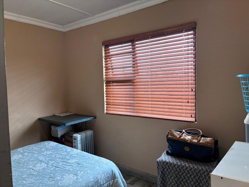 A standard bedroom featuring laminate flooring, coving, and wooden venetian blinds, providing a functional and neutral space.