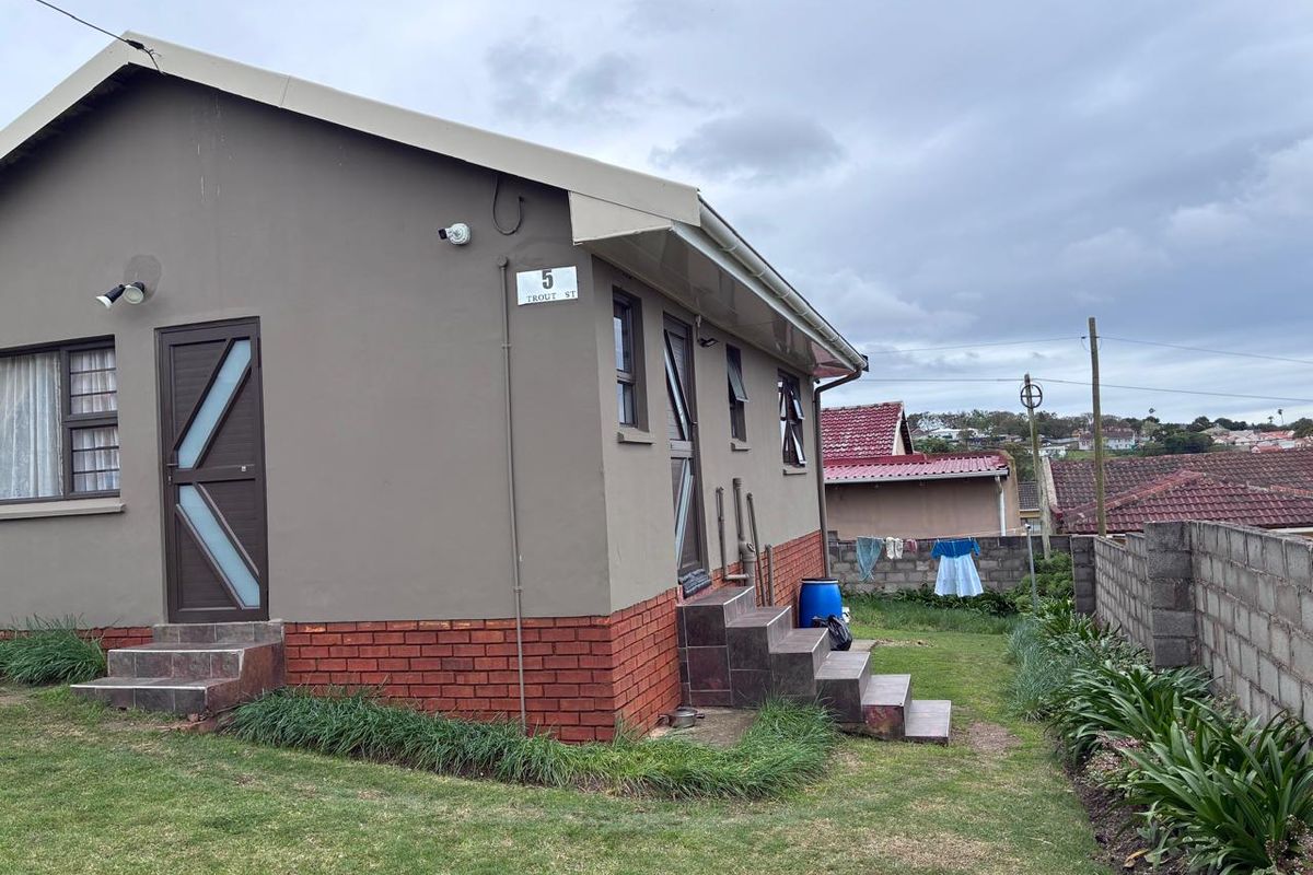 Rear view of the property featuring a brick base, tiled steps, security doors, and a concrete block boundary wall in a residential setting.
