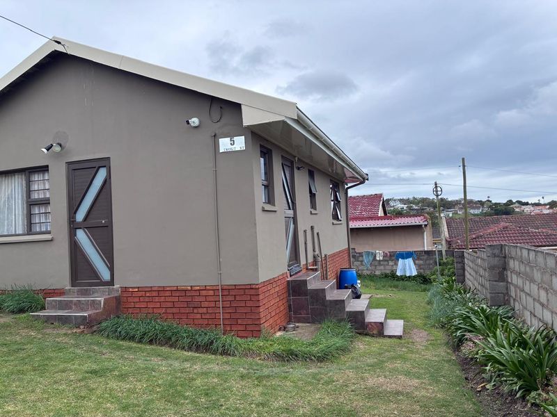 Rear view of the property featuring a brick base, tiled steps, security doors, and a concrete block boundary wall in a residential setting.