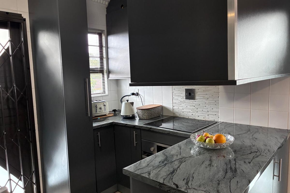 A modern kitchen featuring dark cabinetry, stone countertops, a built-in hob, oven, and extractor fan, complemented by a tiled backsplash.