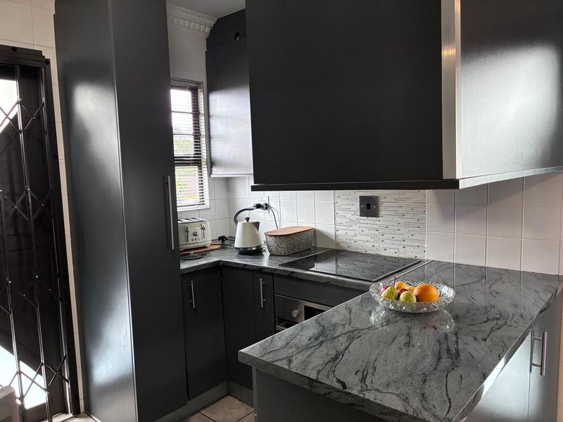 A modern kitchen featuring dark cabinetry, stone countertops, a built-in hob, oven, and extractor fan, complemented by a tiled backsplash.