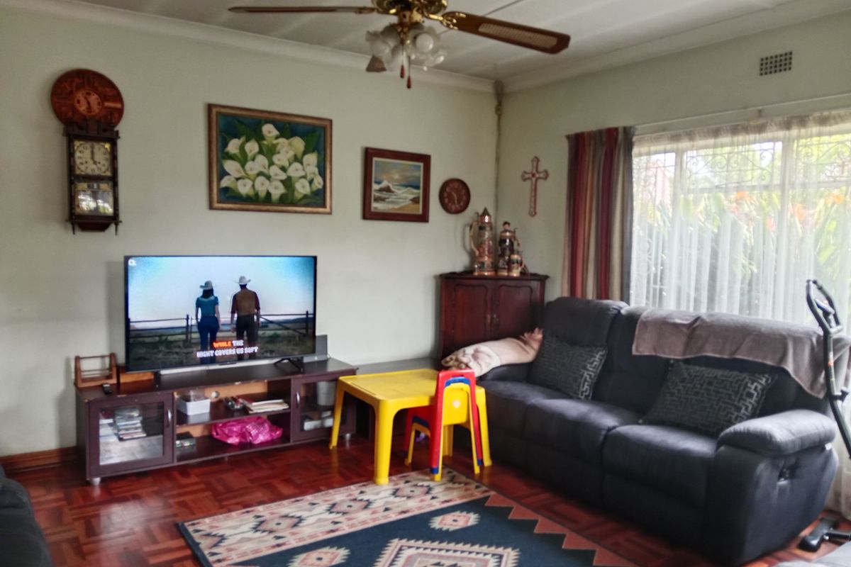 A living room featuring classic parquet flooring, a ceiling fan, and large windows with security bars, offering a comfortable and functional living space.
