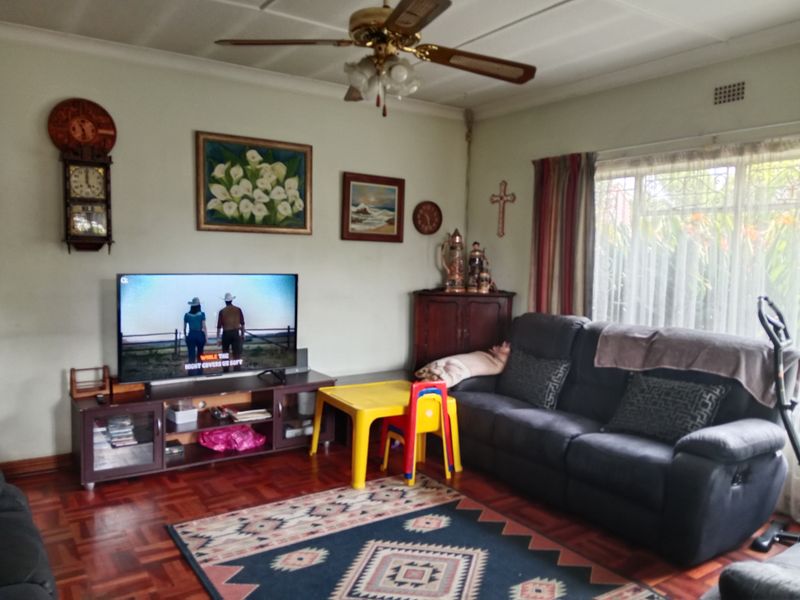 A living room featuring classic parquet flooring, a ceiling fan, and large windows with security bars, offering a comfortable and functional living space.