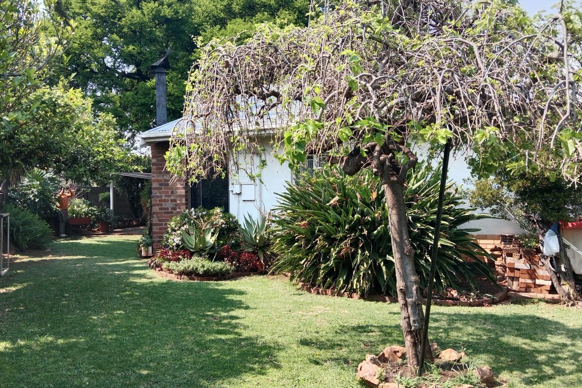 A view of the rear garden featuring a well-maintained lawn, established trees, and a brick-accented exterior wall with a chimney.
