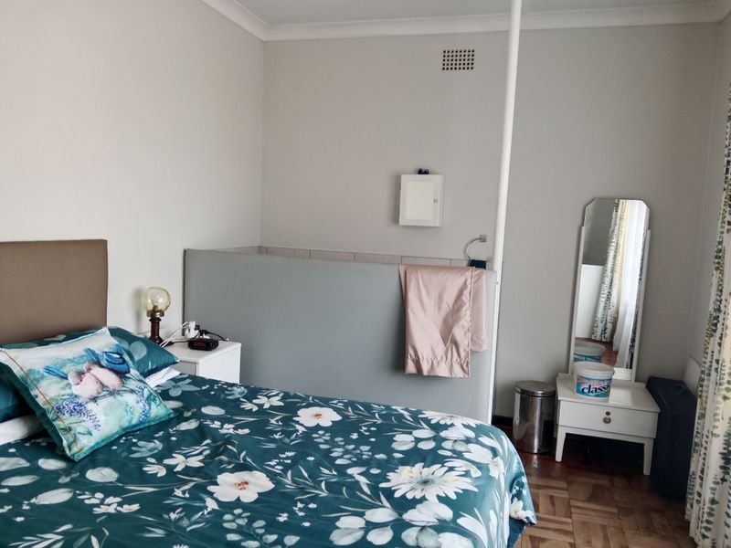 A bedroom featuring parquet flooring and a central partition wall, offering a functional layout with neutral wall finishes.