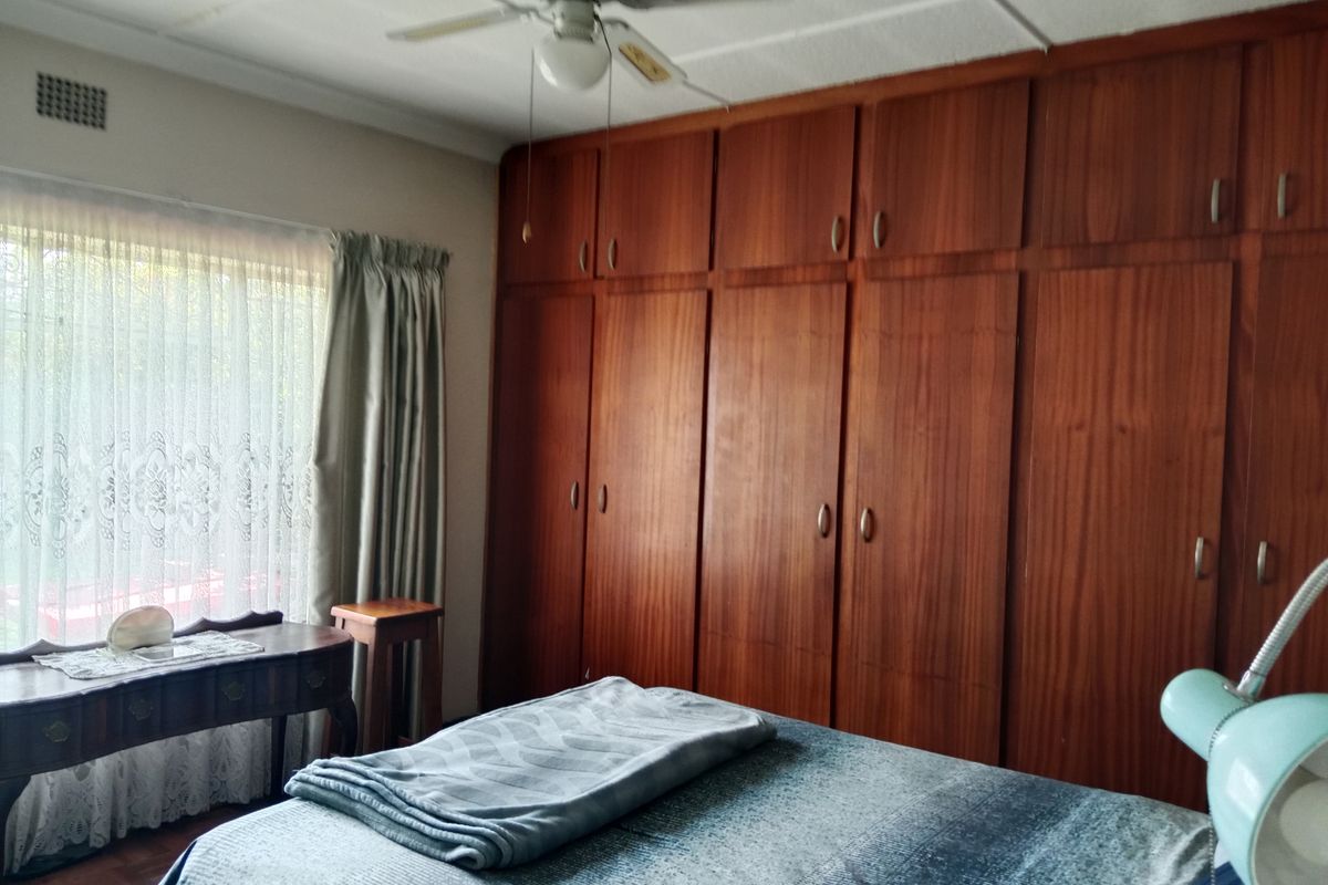A bedroom featuring extensive floor-to-ceiling built-in wooden cabinetry, a ceiling fan, and parquet flooring, offering ample storage space.