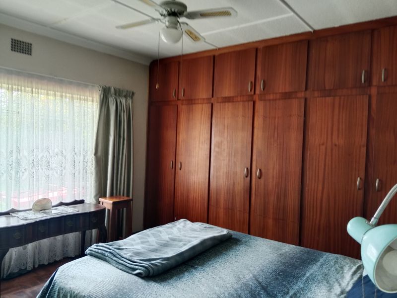 A bedroom featuring extensive floor-to-ceiling built-in wooden cabinetry, a ceiling fan, and parquet flooring, offering ample storage space.