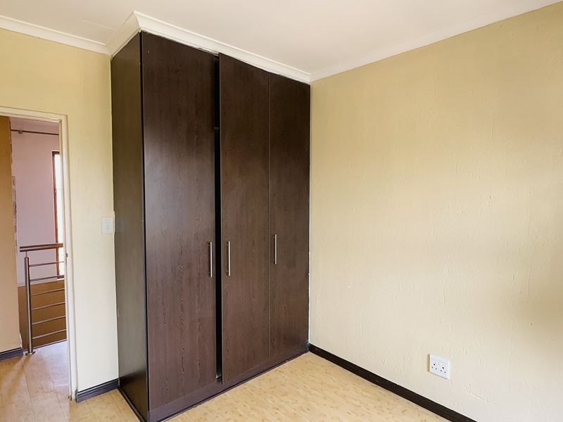 A bright, empty bedroom featuring dark wood built-in wardrobes, laminate flooring, and neutral wall finishes, offering a clean canvas for personalization.