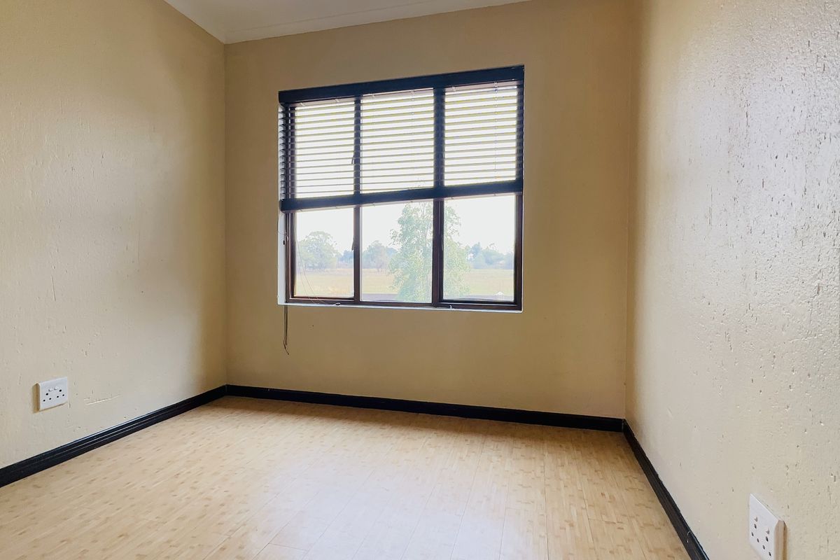 An empty bedroom featuring laminate flooring, neutral walls, and a window with fitted blinds, offering a clean and versatile space.