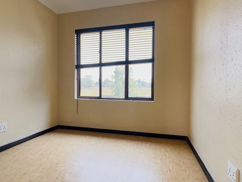 An empty bedroom featuring laminate flooring, neutral walls, and a window with fitted blinds, offering a clean and versatile space.