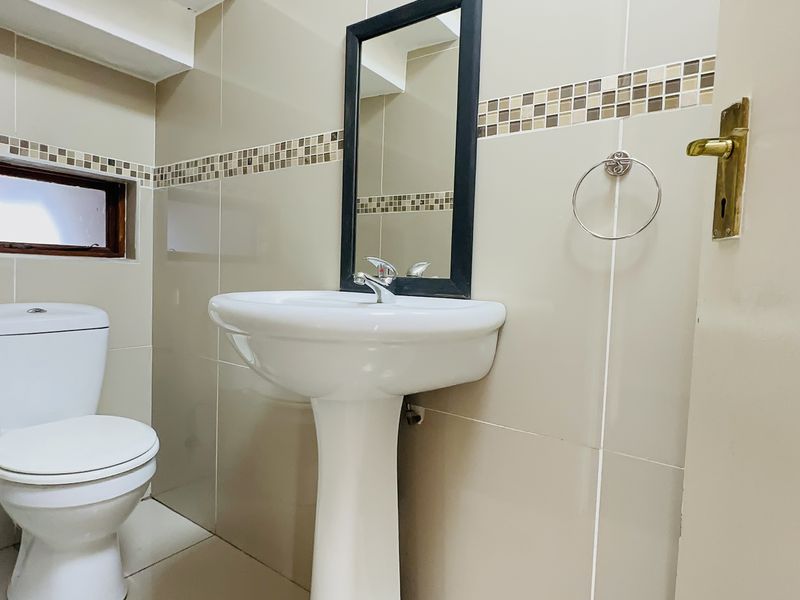 A compact bathroom featuring a pedestal basin, toilet, and neutral wall tiling with a decorative mosaic border.
