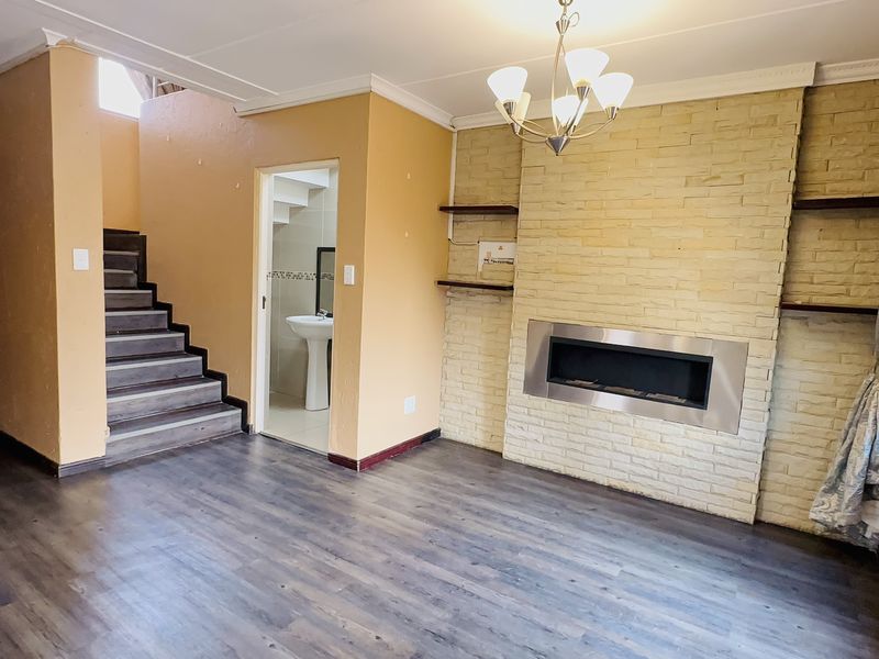 Spacious living room featuring a stone-clad built-in fireplace, laminate flooring, and an adjacent staircase leading to the upper level.