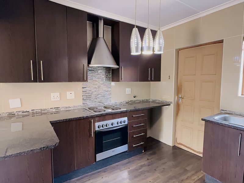A functional kitchen featuring dark wood cabinetry, granite countertops, a built-in oven with extractor fan, and a double basin sink.