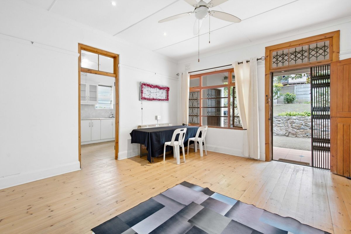 Spacious living area featuring polished timber flooring, ceiling fan, and direct access to the outdoor area, with an adjoining kitchen space.
