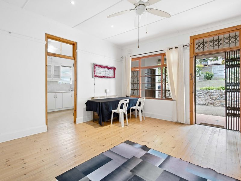 Spacious living area featuring polished timber flooring, ceiling fan, and direct access to the outdoor area, with an adjoining kitchen space.