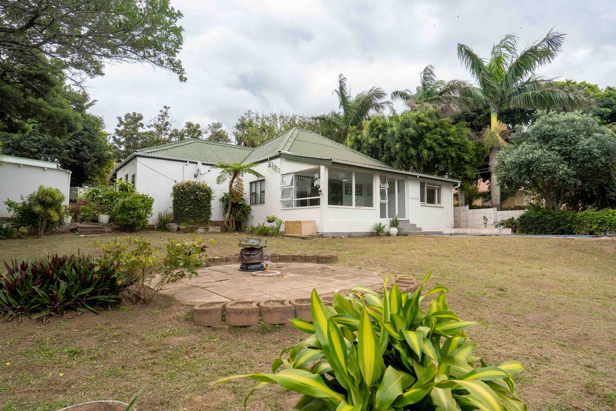 Rear view of the house featuring a metal roof, white exterior facade, and a spacious garden with a paved patio area.