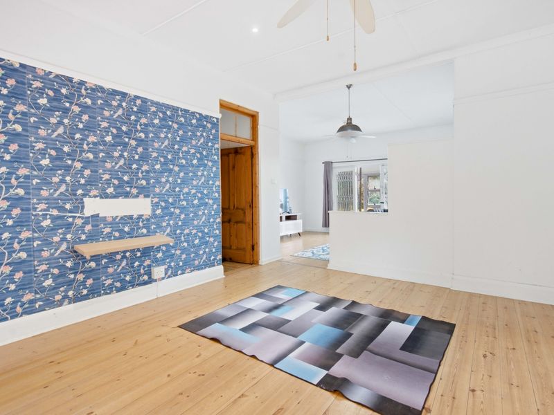 Spacious living area featuring polished timber flooring, a ceiling fan, and a decorative feature wall, offering a bright and open layout.