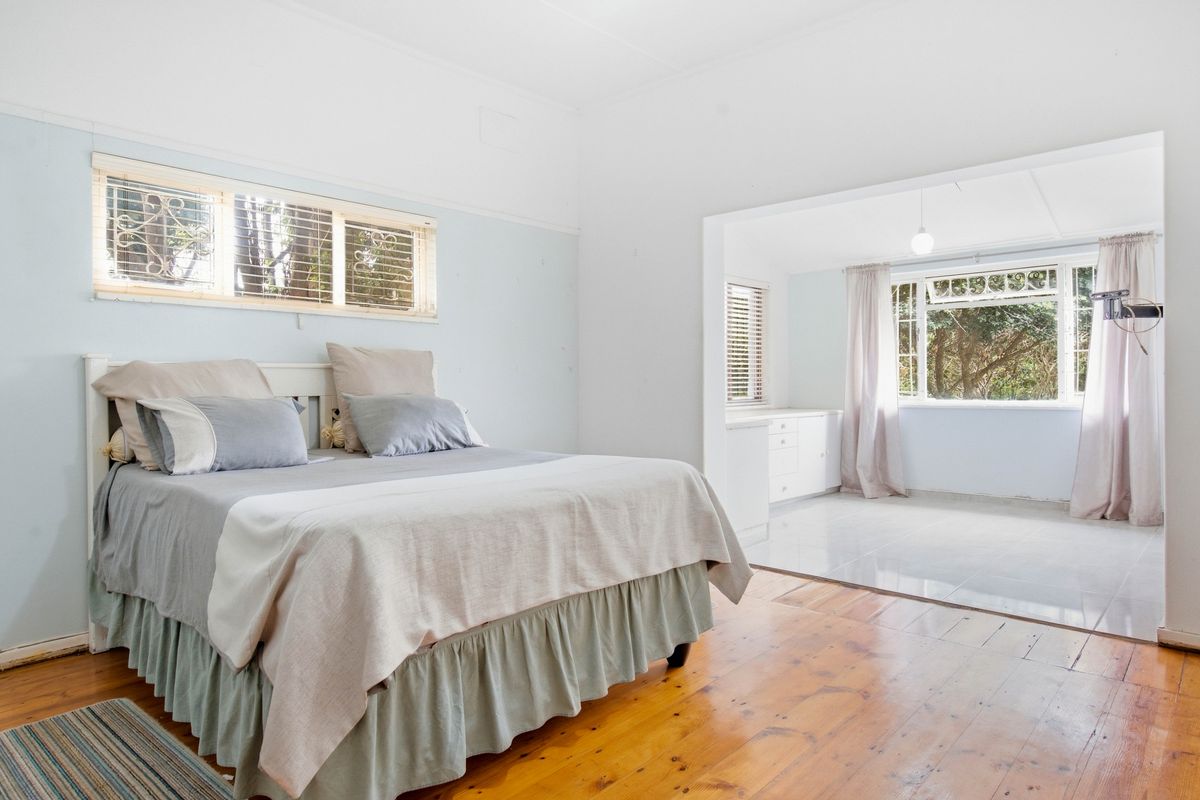 Spacious bedroom featuring polished timber floors, an adjoining sunroom or study area with tiled flooring, and large windows providing natural light.