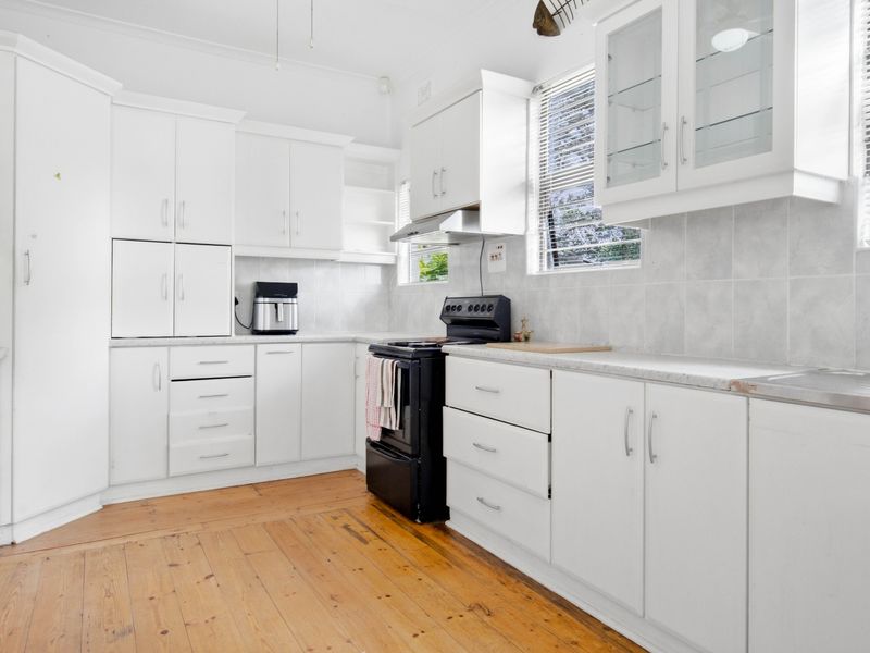 A functional kitchen featuring white cabinetry, tiled backsplash, timber flooring, and a freestanding stove with an extractor fan.