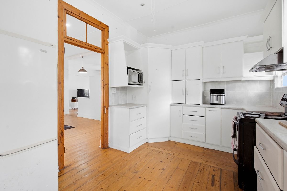 A functional kitchen featuring white cabinetry, timber flooring, and a built-in microwave, with a view through a timber-framed doorway into the adjacent living area.