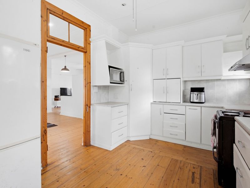 A functional kitchen featuring white cabinetry, timber flooring, and a built-in microwave, with a view through a timber-framed doorway into the adjacent living area.