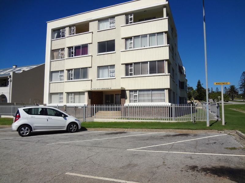 Front elevation of the Knightsbridge apartment building featuring multi-level balconies, security fencing, and an adjacent paved parking area.