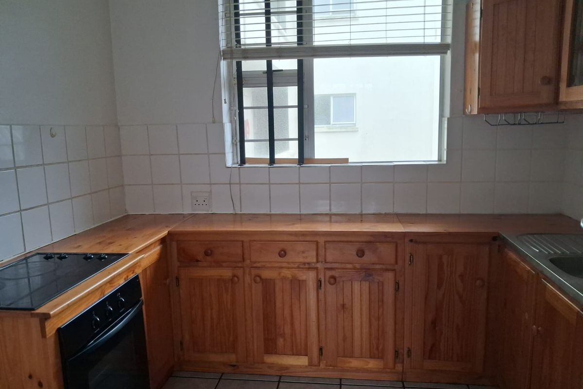 A functional kitchen featuring wooden cabinetry, a built-in oven with electric hob, tiled backsplash, and a stainless steel sink.