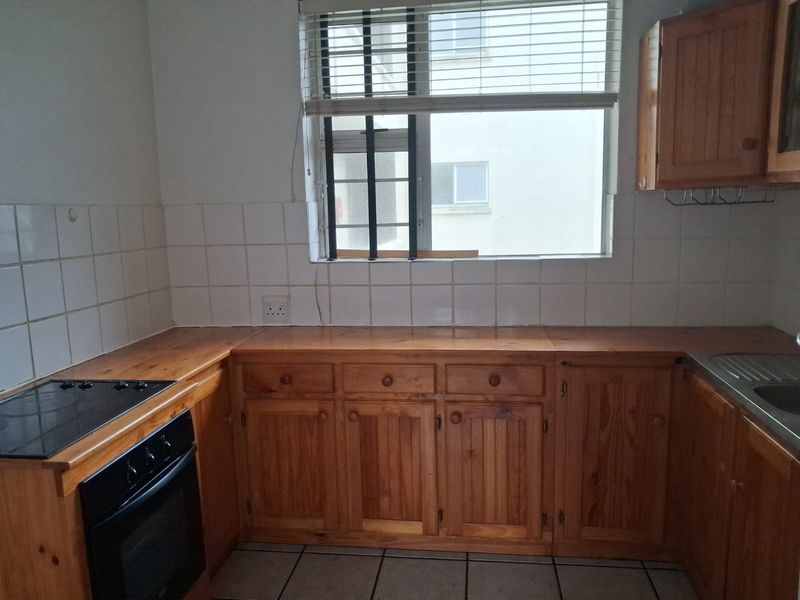 A functional kitchen featuring wooden cabinetry, a built-in oven with electric hob, tiled backsplash, and a stainless steel sink.