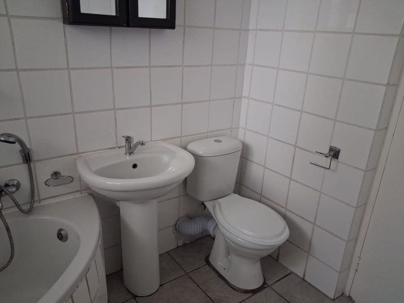 A functional bathroom featuring a pedestal basin, toilet, and bathtub with white wall tiling and tiled flooring.