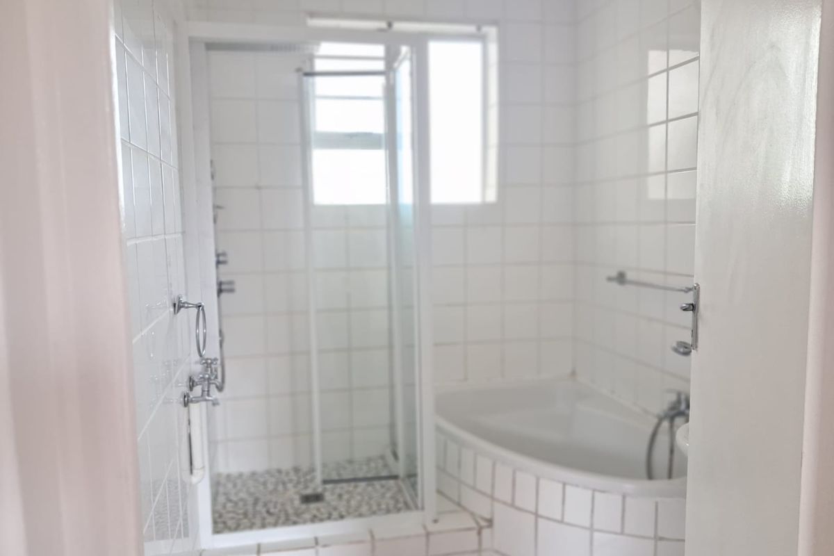 A functional bathroom featuring a built-in bathtub, a separate shower enclosure, and white wall tiling throughout.