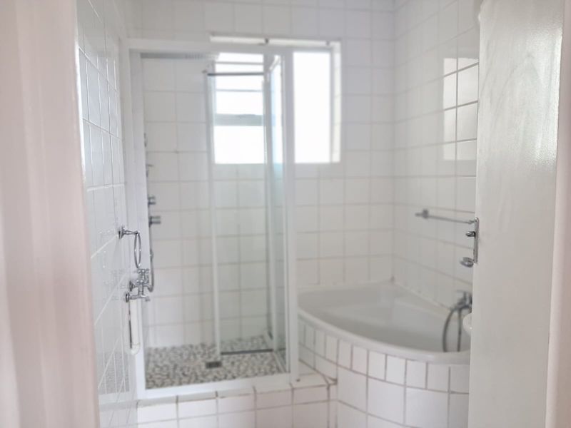 A functional bathroom featuring a built-in bathtub, a separate shower enclosure, and white wall tiling throughout.