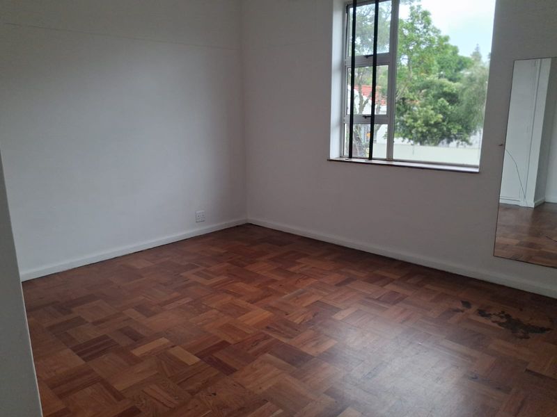 An empty bedroom featuring classic parquet flooring and a window with natural light, providing a blank canvas for interior design.