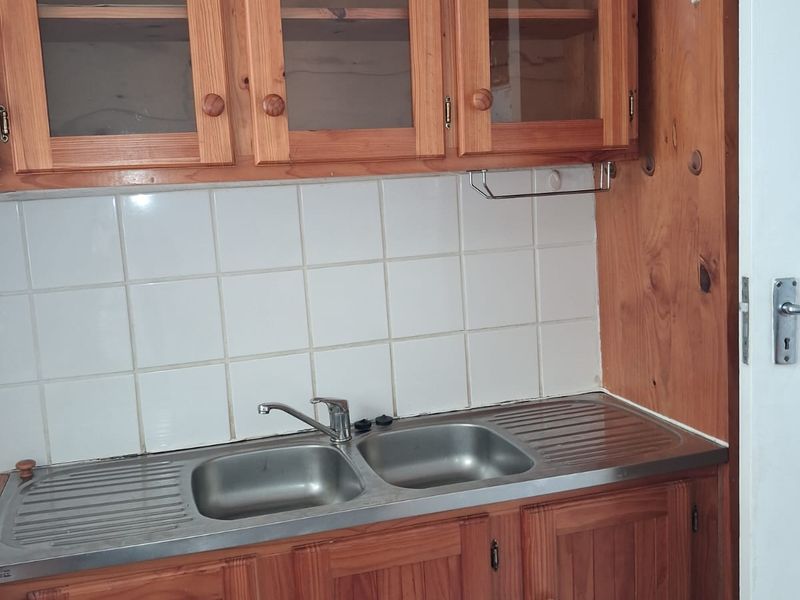 A functional scullery area featuring wooden cabinetry, a double bowl stainless steel sink, and a tiled splashback.