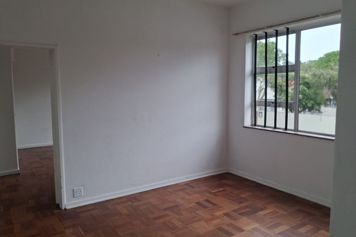 An empty bedroom featuring classic parquet flooring, white walls, and a window fitted with security bars, offering a blank canvas for personalization.